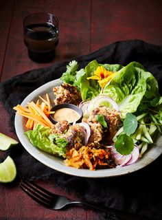 a white plate topped with lettuce, carrots and meatballs next to a fork