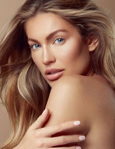 a woman with blonde hair and blue eyes is posing for the camera, her hand on her shoulder