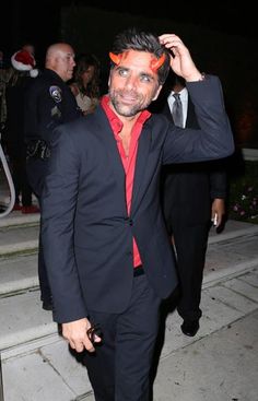 a man in a black suit and red shirt is standing on the steps with his hand up to his head