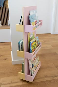 a pink book stand with books in it on the floor next to a stair case