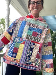 a woman in glasses is holding up a colorful quilt