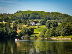 a small boat is on the water in front of a large hill with a house