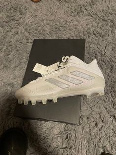 a pair of white adidas soccer cleats on a black box and some shoes