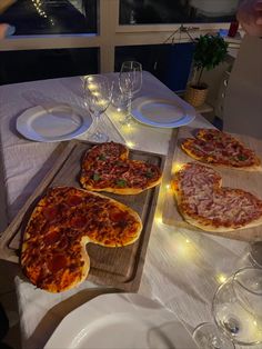 three pizzas on wooden trays sitting on a table with wine glasses and plates