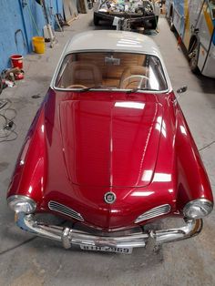 an old red car parked in a garage next to other cars and motorcycles on the street