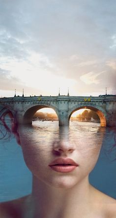 a woman's face is reflected in the water with an old bridge behind her