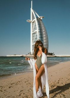 a woman standing on top of a sandy beach next to the ocean wearing a bathing suit