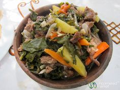 a wooden bowl filled with meat and vegetables on top of a white tablecloth covered table