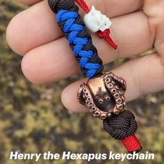 there is a hand holding a bracelet with an octopus on it and a red white and blue cord