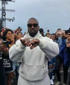 a man in a white hoodie pointing his finger at the camera while people take pictures