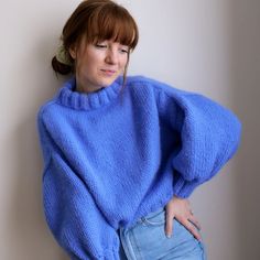 a woman in a blue sweater leaning against a wall with her hands on her hips