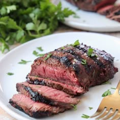 a piece of steak on a white plate with a fork and parsley next to it