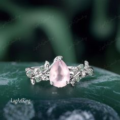 an engagement ring with a pink stone surrounded by white diamonds on top of a green surface