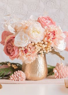 a gold vase filled with pink and white flowers on top of a table next to two forks