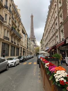 the eiffel tower is seen in the distance from this street lined with parked cars