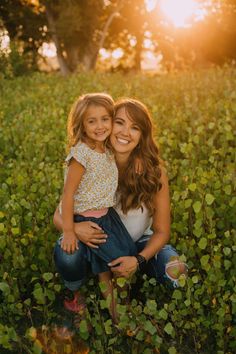 a mother and daughter sitting in the middle of a field with green plants at sunset