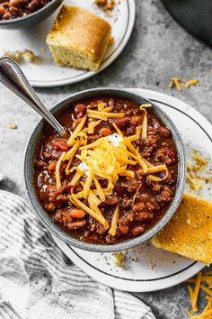 two bowls of chili with cheese and bread on the side