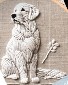 a white dog sitting on top of a table next to a piece of cloth and thread