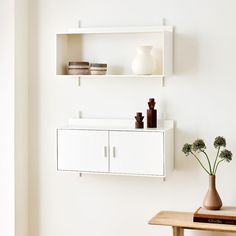 a white shelf with two vases on top of it and some flowers in front of it