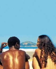 three people sitting on the beach looking out at the ocean