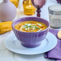 a purple bowl filled with soup on top of a white plate