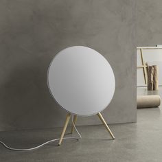 a white round object with wooden legs in front of a gray wall and concrete floor