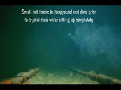 an underwater photo with the caption small rail tracks in foreground and diver prior to crystal clear water still up completely below