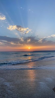 the sun is setting over the ocean with clouds in the sky and waves on the beach