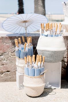 several umbrellas are placed in baskets on the ground next to an umbrella stand with blue and white umbrellas