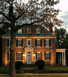 a large brick house with white trim and black shutters on the front door is lit up at night