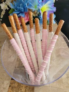 there are six pink and white candy sticks in a glass bowl with flowers on the table