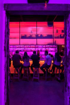 people are sitting at a bar with purple lights on the wall and in front of them