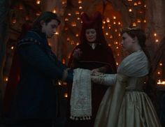 a man and woman dressed in medieval clothing standing next to each other with fairy lights behind them