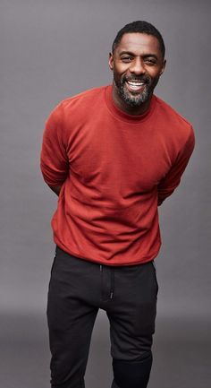 a man in a red shirt and black pants posing for the camera with his hands on his hips