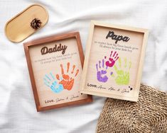 two framed pictures with handprints on them sitting next to a straw hat and pine cone