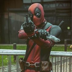 a man dressed as deadpool pointing at something in his hand while standing next to a fence