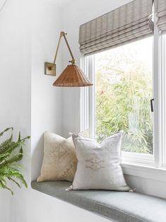 a window sill with two pillows and a lamp on it next to a potted plant