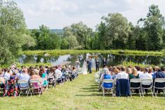 a wedding ceremony in the middle of a field near a pond with people sitting on chairs