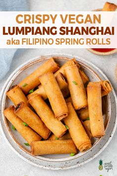 a plate full of fried spring rolls next to dipping sauces on a white surface