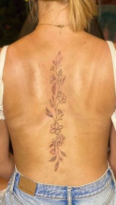 the back of a woman's lower back tattoo with flowers and leaves on it