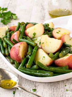 a white bowl filled with green beans and potatoes on top of a table next to a spoon