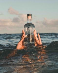 someone holding up a bottle of vodka in the middle of the ocean with their head above the water