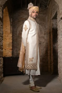 a man dressed in white and gold standing next to an archway