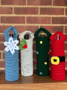 four crocheted bottles sitting on top of a wooden shelf next to a brick wall