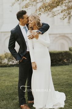 a man and woman standing next to each other in front of a tree with their arms around each other