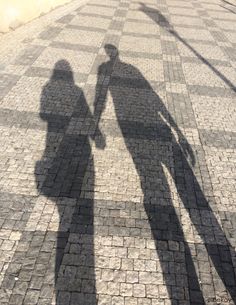 the shadow of two people standing next to each other on a brick road with an umbrella