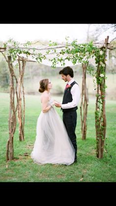 a bride and groom are standing under an arch made out of branches with greenery