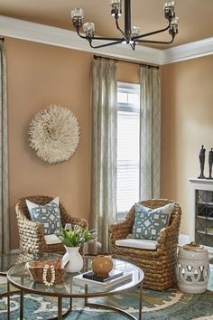 a living room with two chairs and a coffee table in front of a window that has curtains on the windowsill