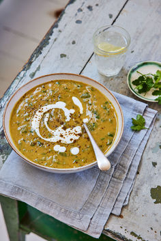 a bowl of soup on a table next to a glass of water and a spoon