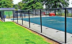 an empty swimming pool behind a fenced in area with green grass and trees on the other side